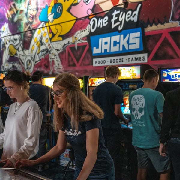 Patrons playing arcade games at One Eyed Jacks bar-and-grill, with colorful wall murals.