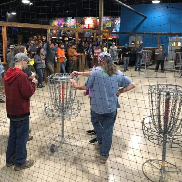 People playing indoor disc golf at One Eyed Jacks, with arcade games in the background.