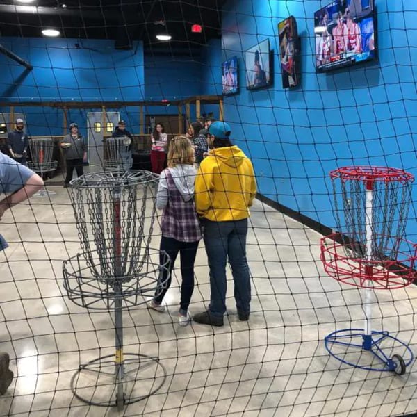 People playing indoor disc golf at One Eyed Jacks, with blue walls and TVs in the background.