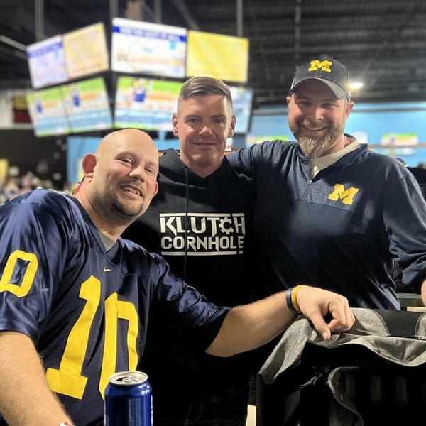 Three men in Michigan sports apparel smiling at One Eyed Jacks bar-&-grill.