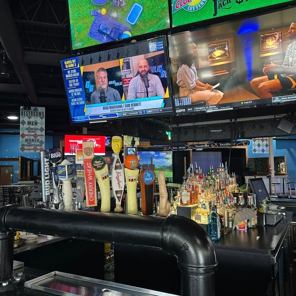 A bar counter with numerous beer taps and liquor bottles, with multiple TVs showing sports and news.