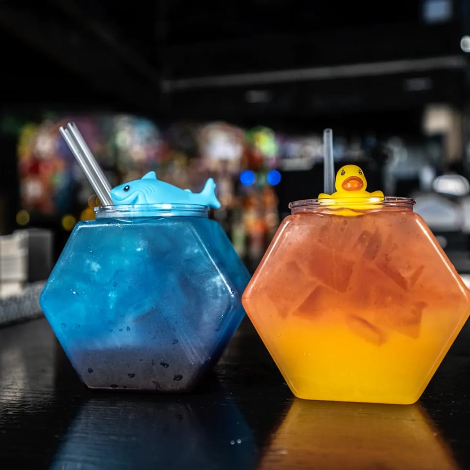 Two hexagonal drinks, one blue with a shark lid, one orange with a rubber duck lid.