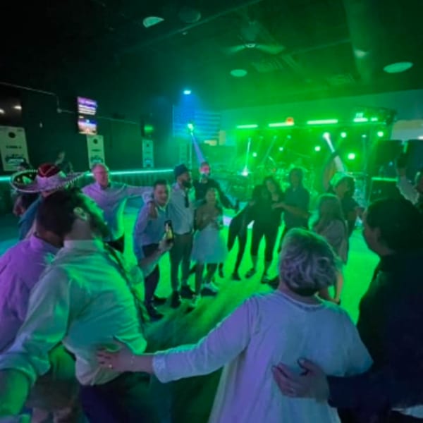 Patrons dancing and socializing under vibrant green and purple lights at One Eyed Jacks bar.