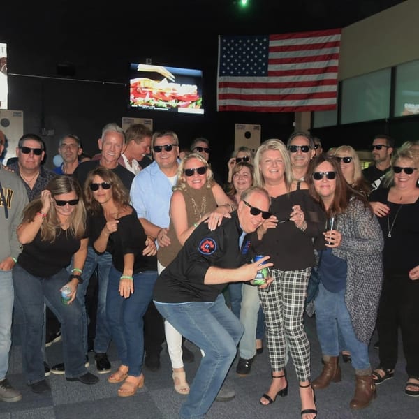 A large group of smiling adults wearing sunglasses poses together at One Eyed Jacks bar.