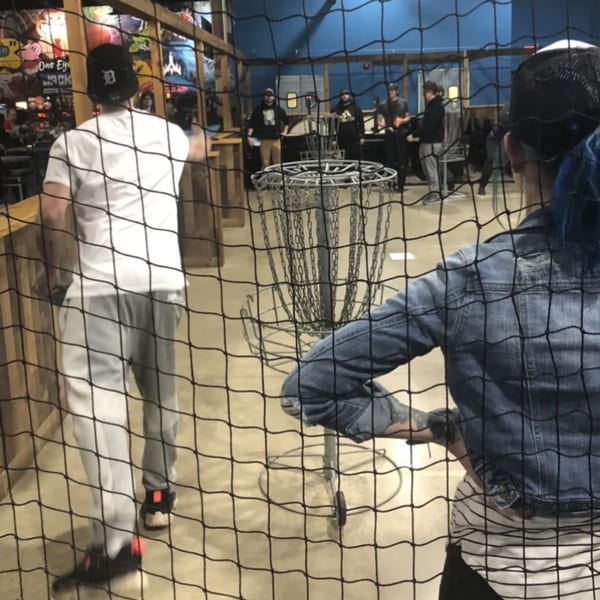People playing indoor disc golf at One Eyed Jacks, viewed through a protective net.