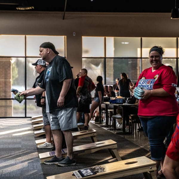 People playing cornhole inside One Eyed Jacks bar-and-grill, with a smiling woman in a red shirt.
