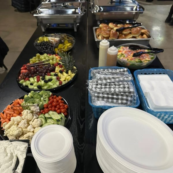 A buffet table with chafing dishes, fruit and vegetable platters, salad, and stacks of plates.