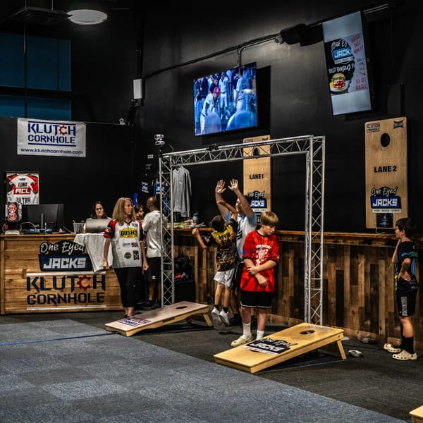People playing cornhole at One Eyed Jacks, with a large TV screen and branded signage.