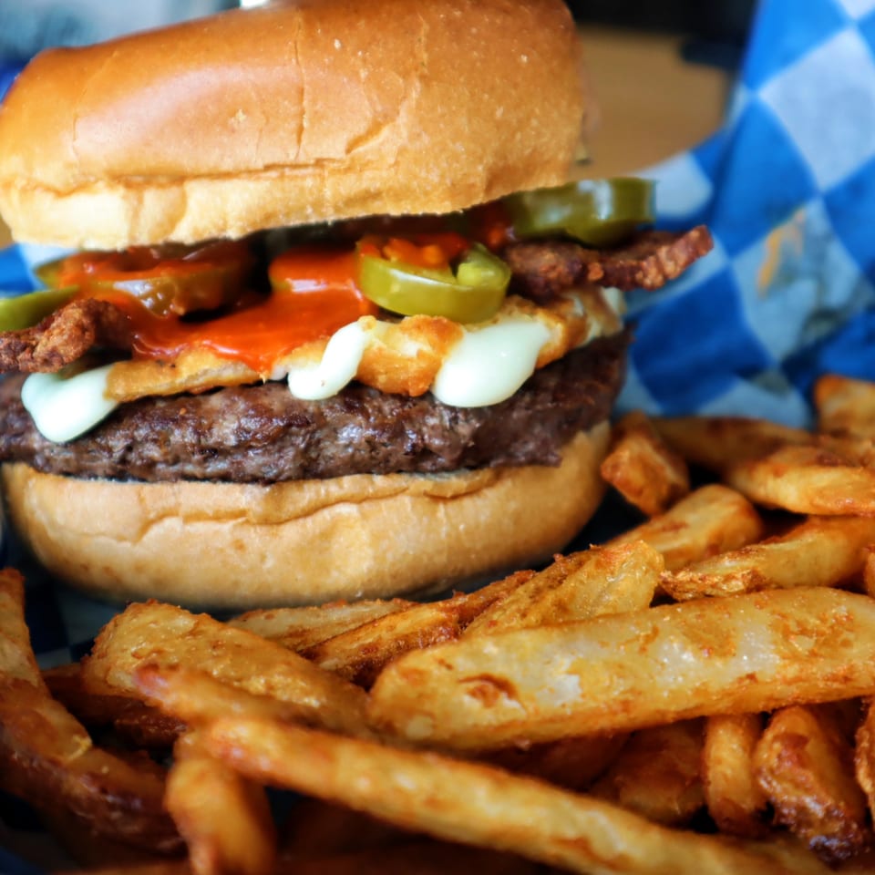 A One Eyed Jacks burger with jalapeños, sauce, and cheese, served with crispy fries.