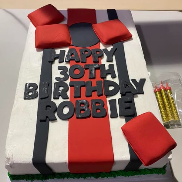 A rectangular birthday cake decorated in black, white, and red, with "Happy 30th Birthday Robbie" in black fondant.