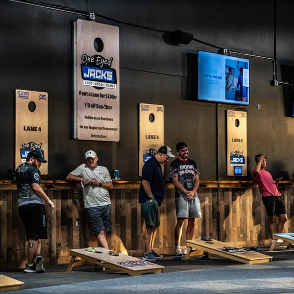 Men play cornhole at One Eyed Jacks, a bar-and-grill with games and screens.