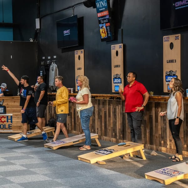 People playing cornhole at One Eyed Jacks, a bar-and-grill with multiple lanes and screens.