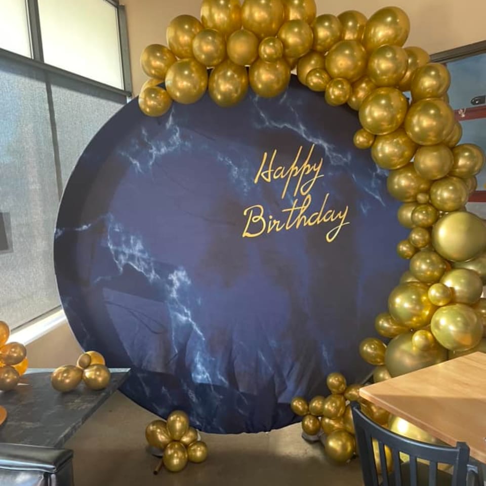 A circular blue marble-patterned backdrop with "Happy Birthday" in gold, framed by gold balloons.