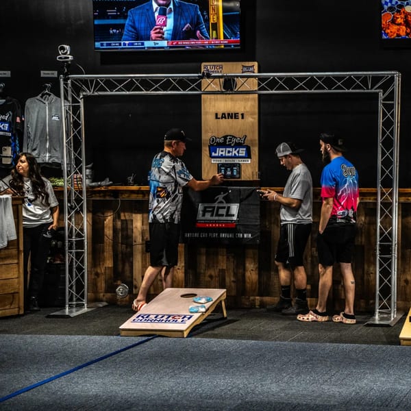 People playing cornhole at One Eyed Jacks, a bar-and-grill, with a TV showing sports above.