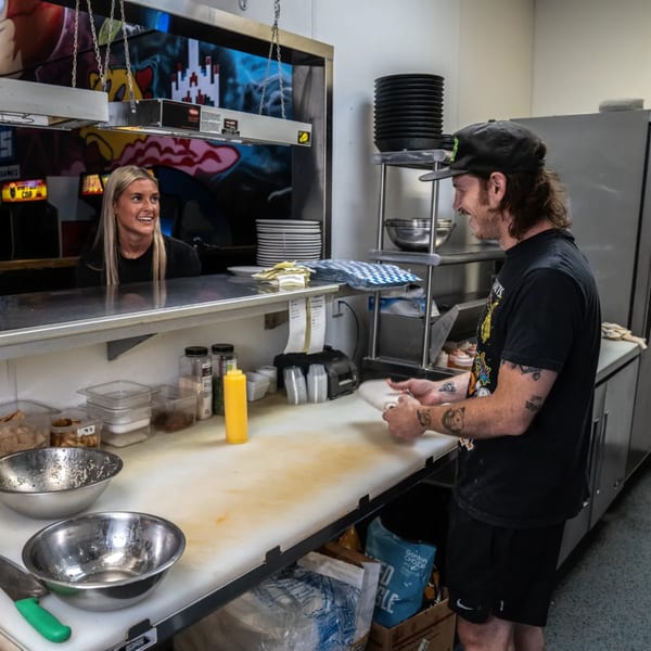 One Eyed Jacks kitchen staff, a man and woman, smiling while working behind the counter.