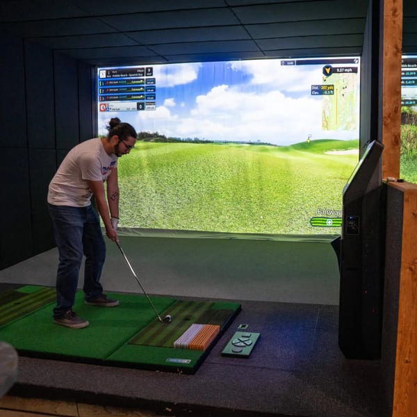 A man plays golf on a simulator at One Eyed Jacks, with a virtual fairway displayed.
