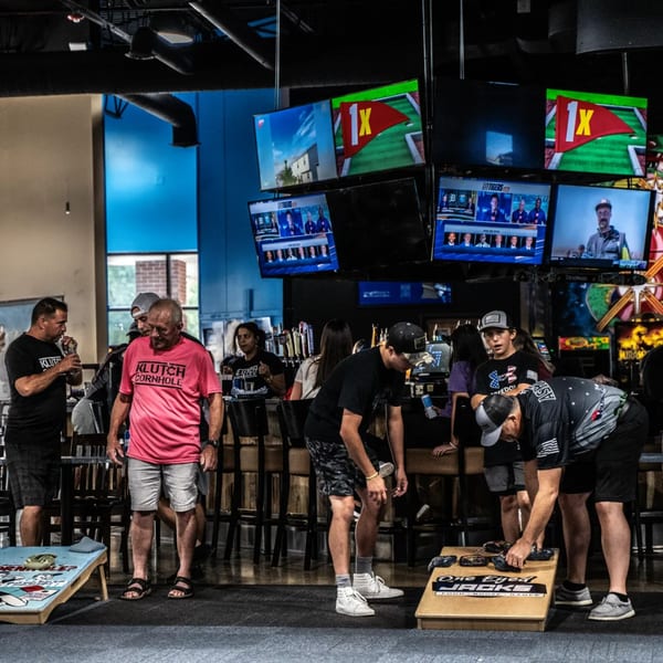 Patrons playing cornhole and watching sports on multiple TVs at One Eyed Jacks bar-and-grill.