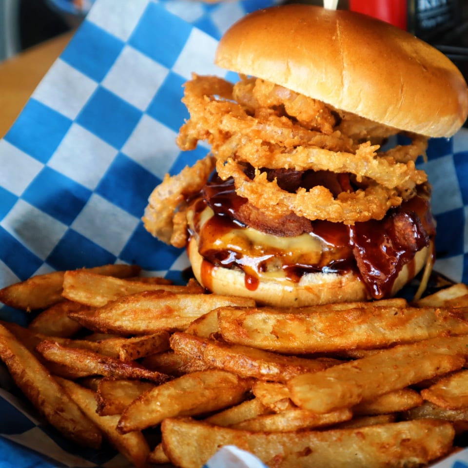 A One Eyed Jacks burger with onion rings and BBQ sauce, served with a side of fries.
