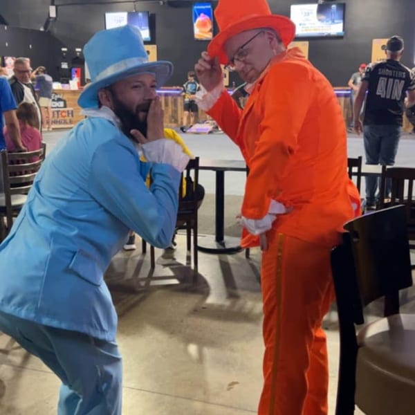 Two men in blue and orange Dumb and Dumber costumes pose playfully inside One Eyed Jacks.