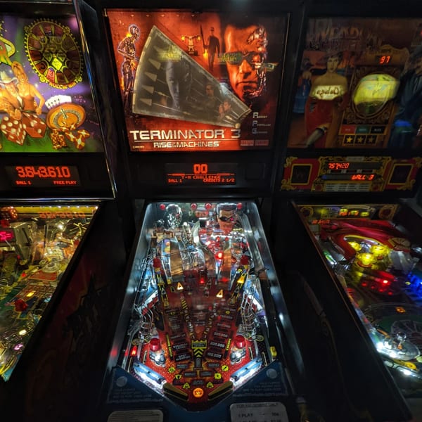 Three pinball machines, including a "Terminator 3" themed game, brightly lit in a bar-and-grill.