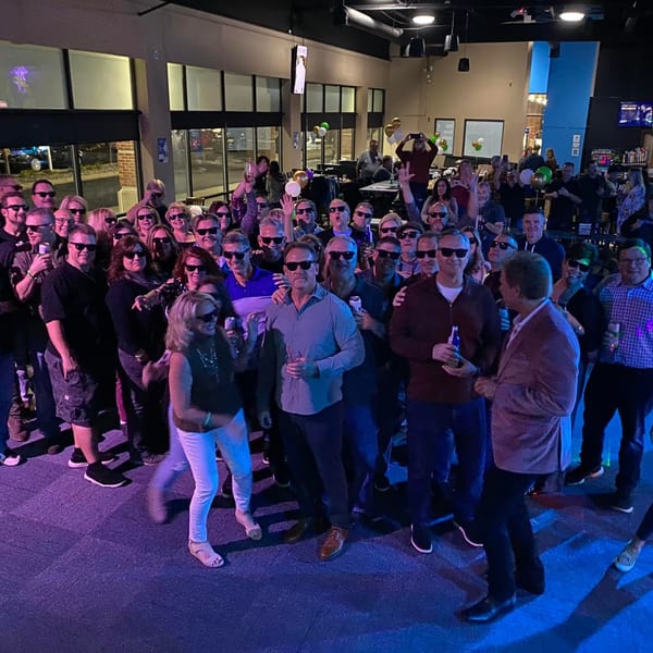A large group of people wearing sunglasses and holding drinks, posing for a photo at One Eyed Jacks.
