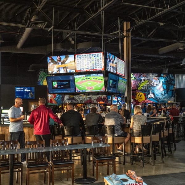 Patrons at One Eyed Jacks bar-&-grill watching sports on multiple large screens above the bar.