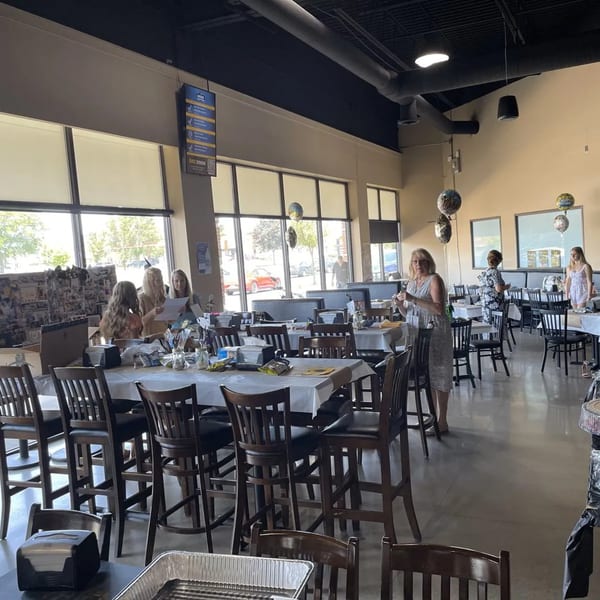 A bright, spacious bar-and-grill dining area with tall tables, chairs, and several women gathered.