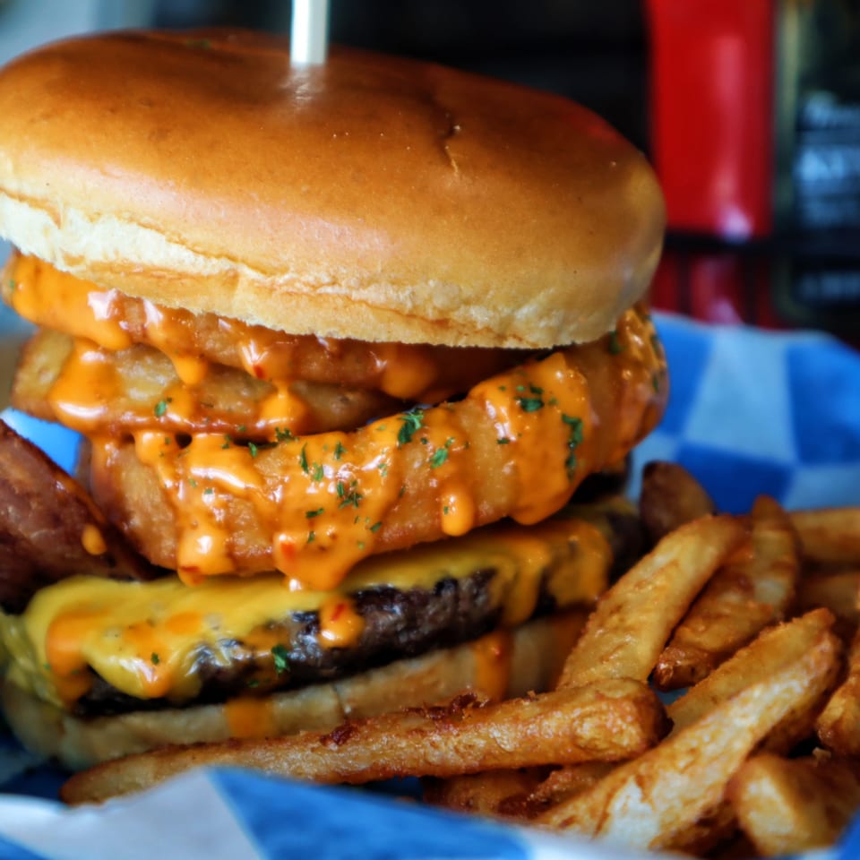 One Eyed Jacks' double cheeseburger with onion rings, spicy sauce, and a side of fries.