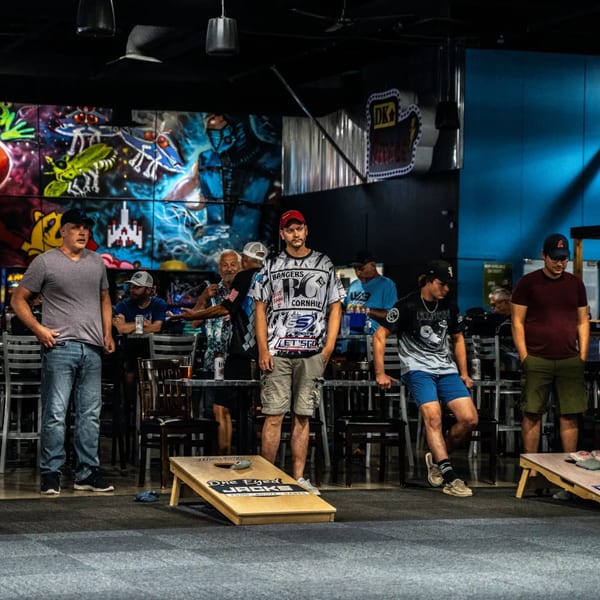 Men playing cornhole inside One Eyed Jacks bar-and-grill with colorful graffiti walls.