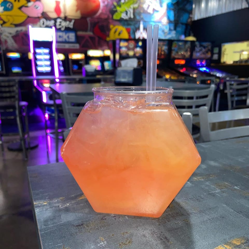 A large, hexagonal, orange drink with ice and two straws sits on a table at One Eyed Jacks.