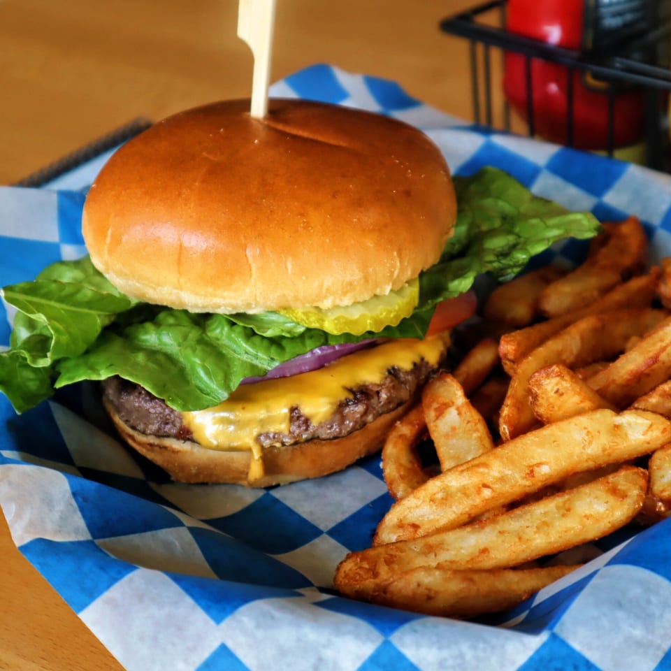 Cheeseburger with lettuce, onion, pickles, and a side of steak fries in a blue checkered basket.