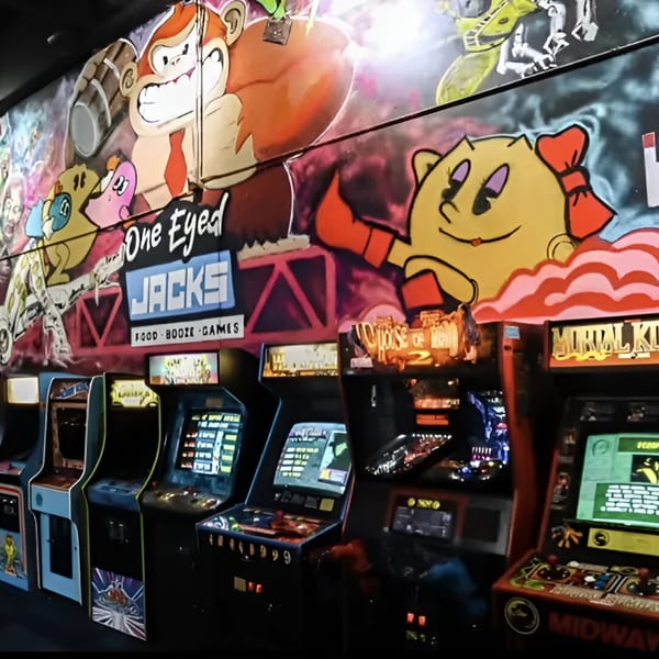 Arcade games line a wall with a colorful mural of classic video game characters like Donkey Kong and Ms. Pac-Man.